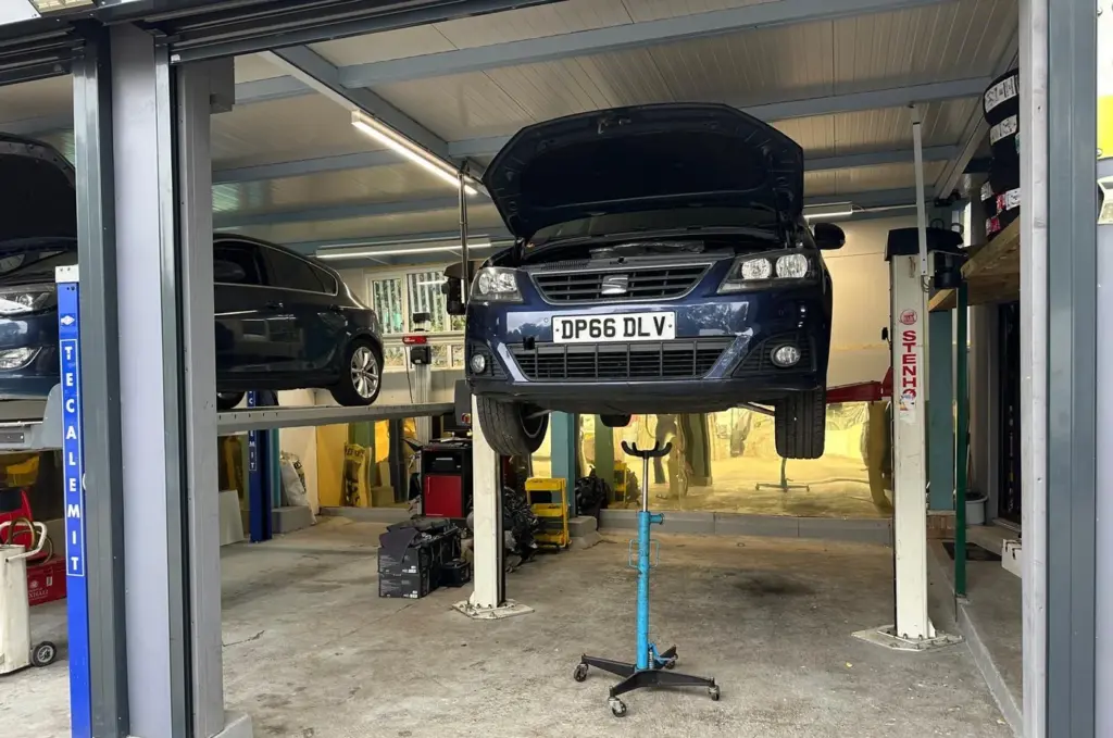A car raised on the two post ramp at AMD Tyres with a transmission jack underneath